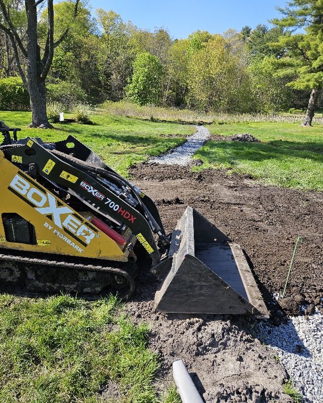 Compact track loader grading a drainage trench on a lawn